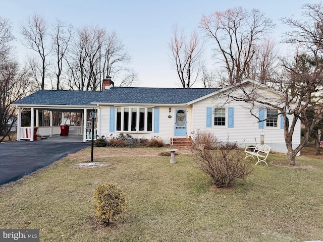 ranch-style house with a carport, aphalt driveway, a chimney, and a front yard