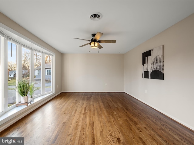 spare room with a ceiling fan, wood finished floors, visible vents, and baseboards