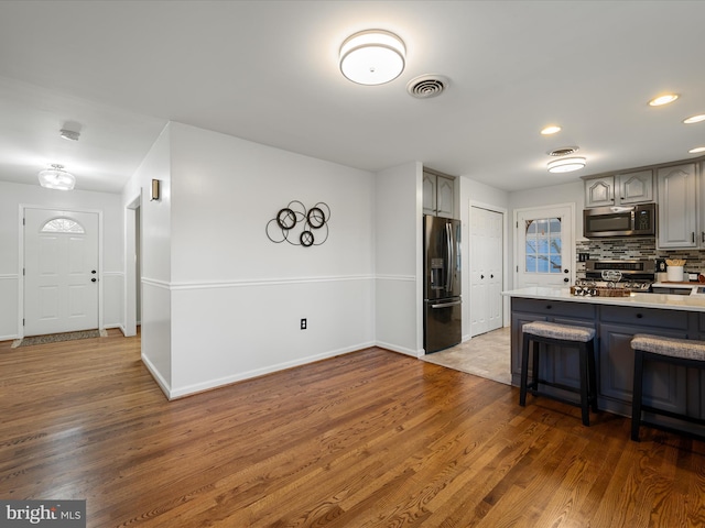 kitchen with visible vents, gray cabinets, backsplash, wood finished floors, and appliances with stainless steel finishes