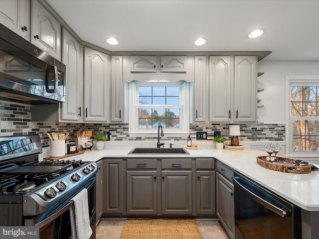 kitchen featuring open shelves, a sink, gray cabinetry, dishwasher, and stainless steel gas stove