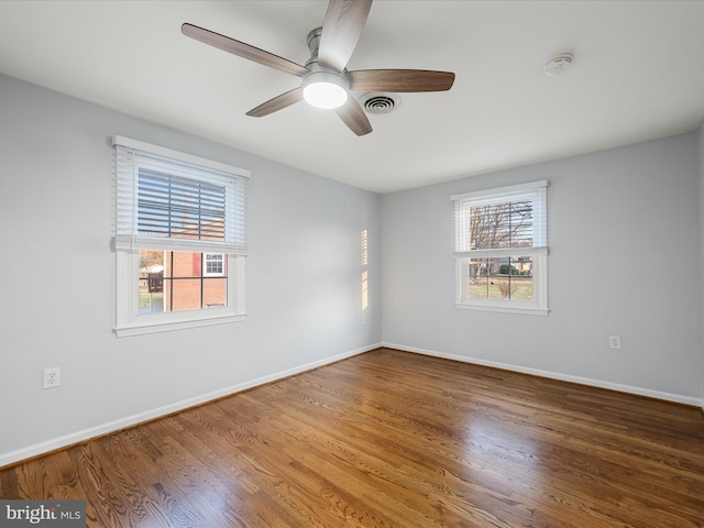 empty room featuring a wealth of natural light, visible vents, and wood finished floors