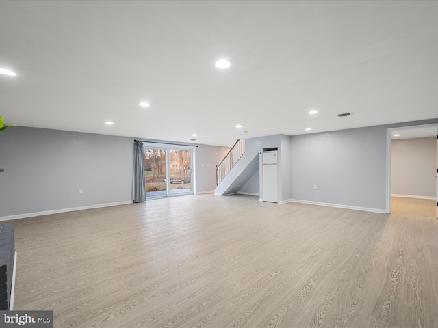 below grade area featuring recessed lighting, baseboards, light wood-style floors, and stairs