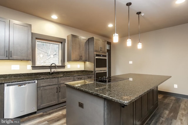 kitchen featuring stainless steel appliances, a kitchen island, dark stone countertops, and a sink