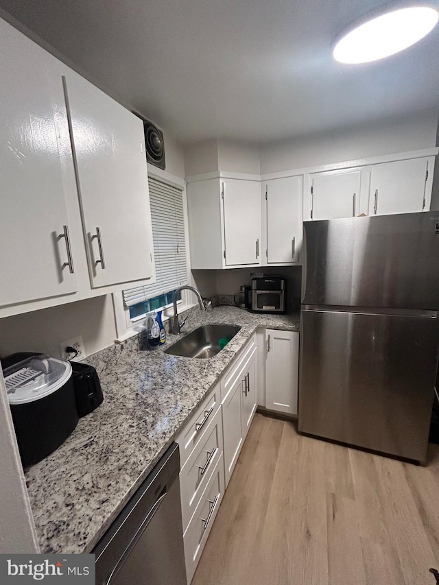 kitchen with light wood-type flooring, white cabinets, stainless steel appliances, light stone countertops, and sink