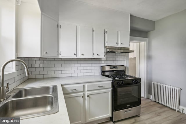 kitchen featuring radiator heating unit, stainless steel gas stove, tasteful backsplash, white cabinetry, and sink