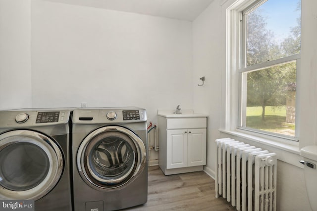 washroom with radiator, sink, light hardwood / wood-style flooring, cabinets, and separate washer and dryer