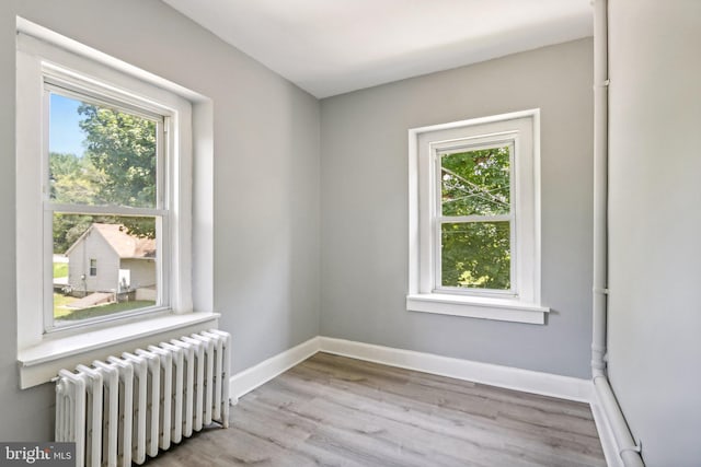 unfurnished room featuring plenty of natural light, radiator, and light hardwood / wood-style floors