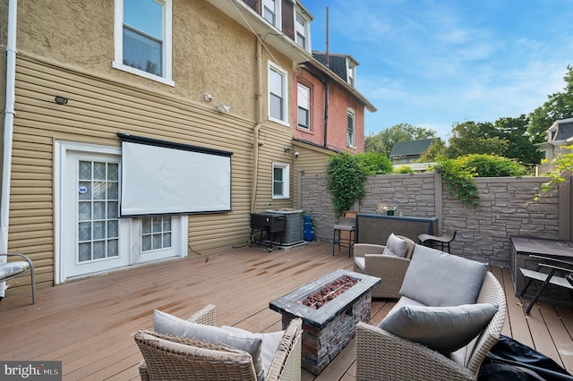 wooden terrace featuring central air condition unit and an outdoor living space with a fire pit