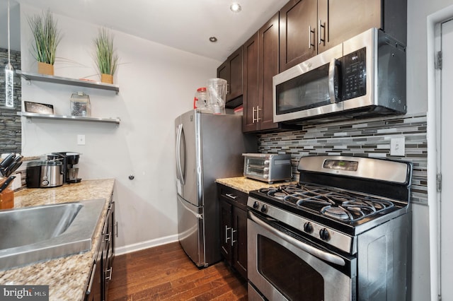 kitchen featuring dark brown cabinetry, decorative backsplash, light stone countertops, and appliances with stainless steel finishes