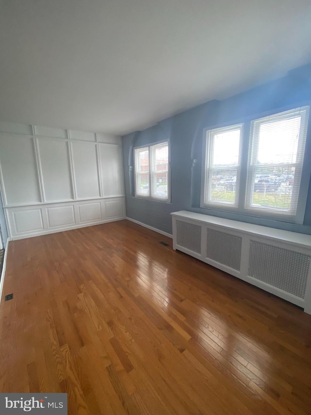 unfurnished bedroom featuring multiple windows, radiator heating unit, and hardwood / wood-style flooring