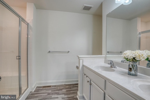 bathroom featuring double sink vanity, a shower with shower door, and wood-type flooring