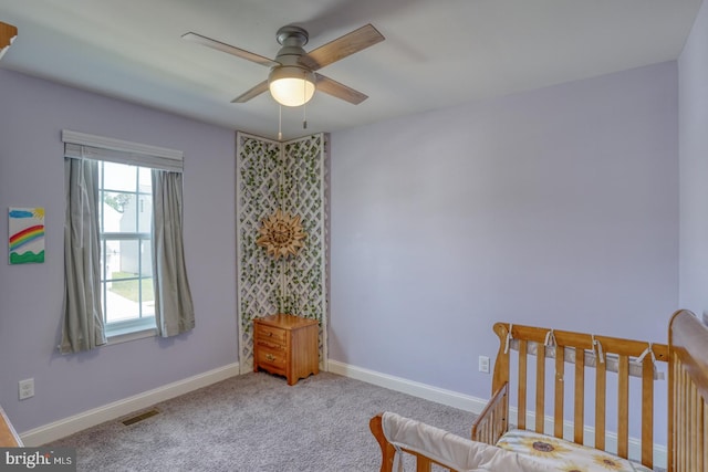 carpeted bedroom featuring ceiling fan and a crib