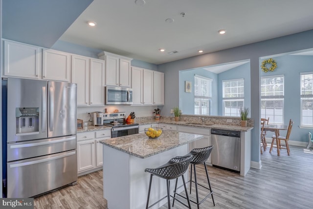 kitchen with appliances with stainless steel finishes, light hardwood / wood-style floors, white cabinetry, light stone countertops, and a center island