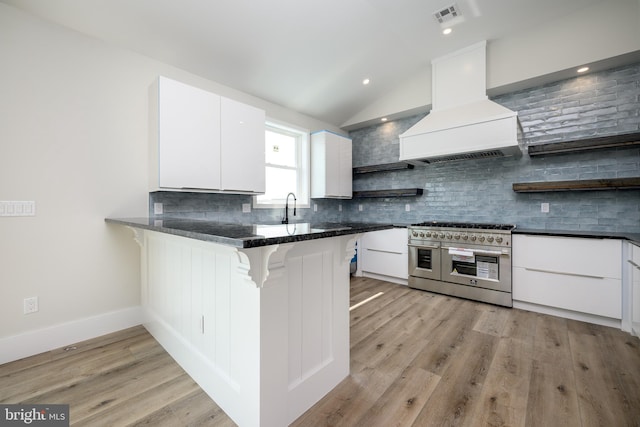 kitchen with range with two ovens, a peninsula, white cabinetry, custom exhaust hood, and open shelves