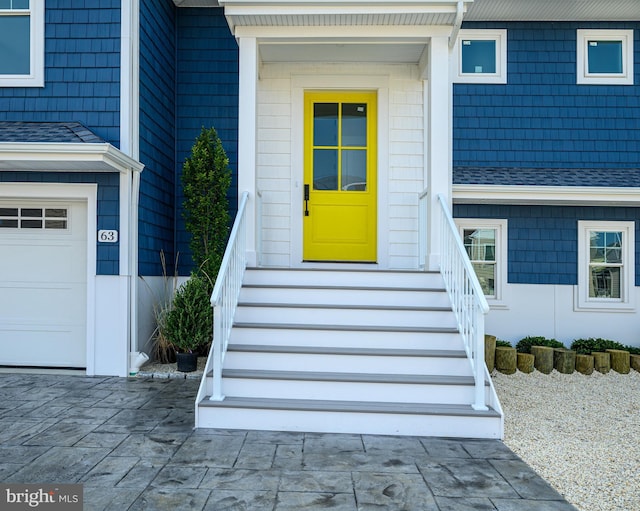 doorway to property with a garage and a shingled roof