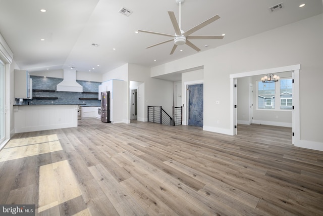 unfurnished living room featuring light wood-type flooring, visible vents, and vaulted ceiling