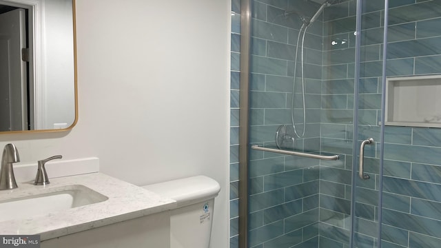 bathroom featuring a shower with door, vanity, and toilet