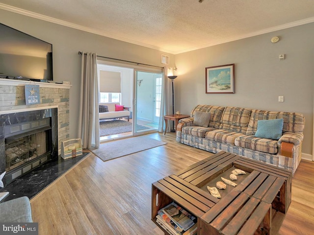 living room with a textured ceiling, crown molding, a stone fireplace, and light hardwood / wood-style flooring