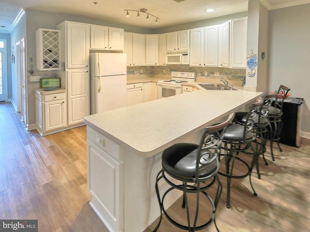 kitchen featuring a breakfast bar area, light hardwood / wood-style flooring, white appliances, and white cabinetry