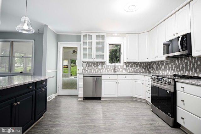 kitchen featuring tasteful backsplash, white cabinetry, appliances with stainless steel finishes, and decorative light fixtures