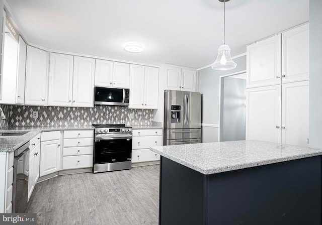 kitchen featuring appliances with stainless steel finishes, pendant lighting, white cabinets, light stone countertops, and light wood-type flooring