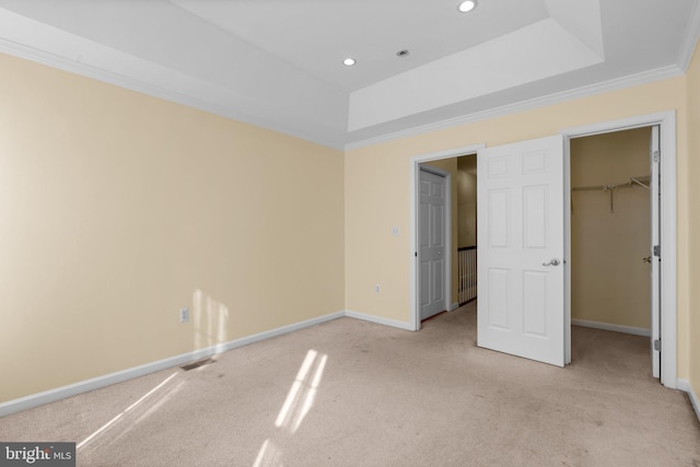 unfurnished bedroom featuring a walk in closet, ornamental molding, a tray ceiling, light colored carpet, and a closet