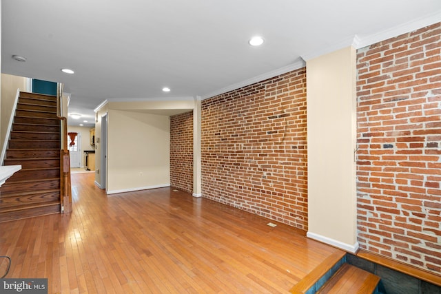 unfurnished living room featuring hardwood / wood-style floors, crown molding, and brick wall