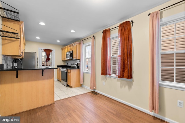 kitchen with backsplash, kitchen peninsula, light hardwood / wood-style floors, a breakfast bar area, and appliances with stainless steel finishes