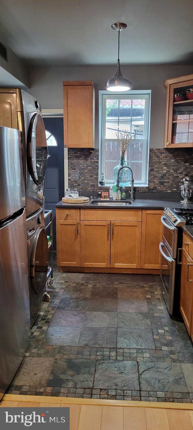 kitchen with appliances with stainless steel finishes, backsplash, sink, dark tile patterned floors, and stacked washer / drying machine