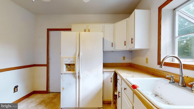 kitchen with sink, white cabinetry, white refrigerator with ice dispenser, and light tile patterned floors