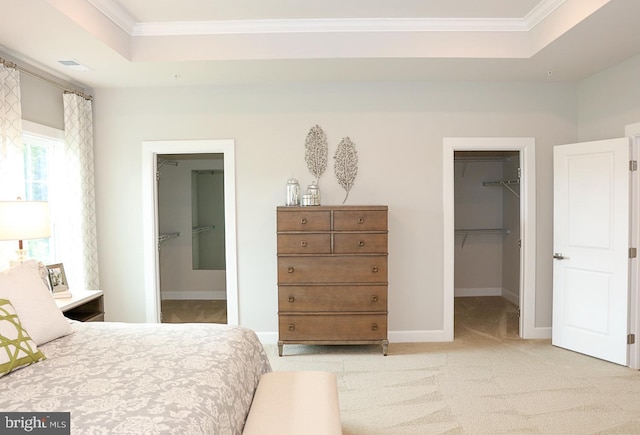 bedroom featuring light carpet, ornamental molding, a closet, a raised ceiling, and a walk in closet