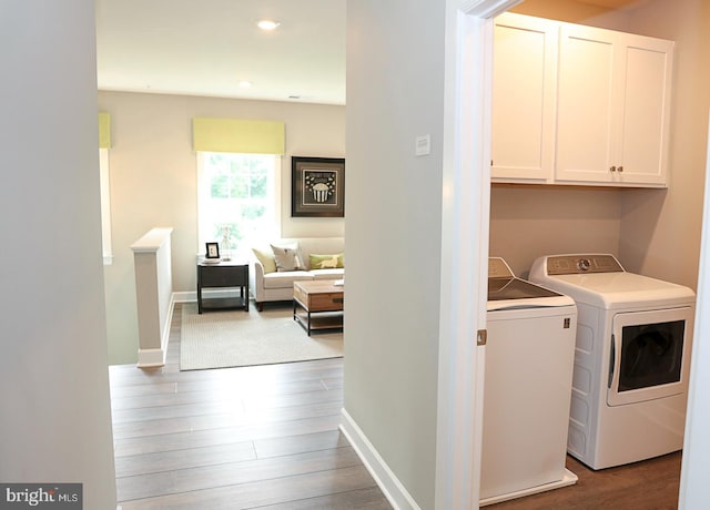 clothes washing area featuring hardwood / wood-style flooring, cabinets, and separate washer and dryer