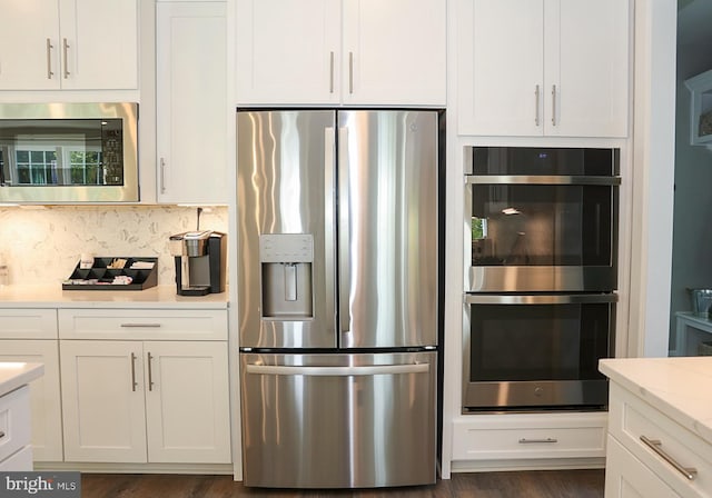 kitchen with tasteful backsplash, stainless steel appliances, light stone counters, dark wood-type flooring, and white cabinets