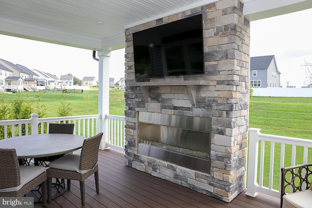 wooden deck with an outdoor stone fireplace and a lawn