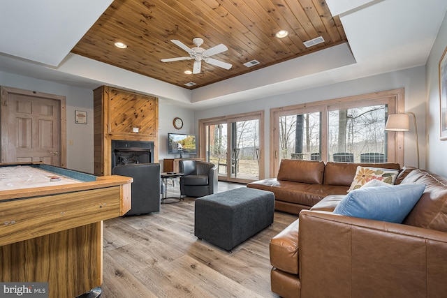 living room with light wood-type flooring, wooden ceiling, a raised ceiling, a fireplace, and ceiling fan