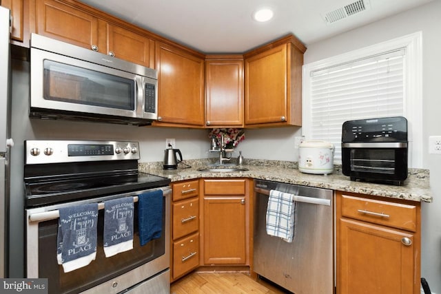 kitchen with light stone counters, light wood-type flooring, stainless steel appliances, and sink