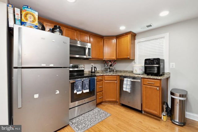 kitchen featuring light stone counters, stainless steel appliances, and light hardwood / wood-style flooring