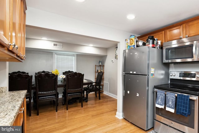 kitchen with stainless steel appliances, light hardwood / wood-style flooring, and light stone counters