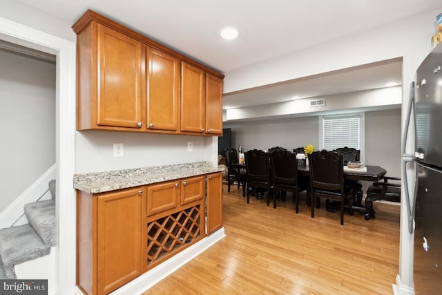 kitchen with light stone countertops, light hardwood / wood-style flooring, and stainless steel refrigerator