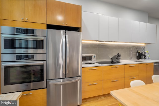 kitchen featuring light wood-type flooring, stainless steel appliances, backsplash, and sink