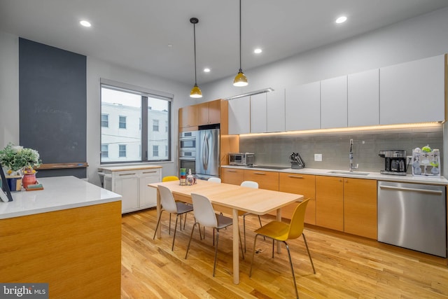 kitchen with stainless steel appliances, light hardwood / wood-style floors, white cabinets, decorative light fixtures, and tasteful backsplash