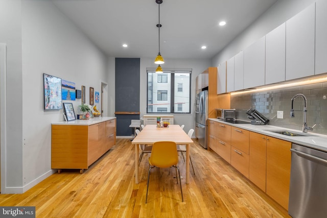 kitchen featuring appliances with stainless steel finishes, backsplash, white cabinetry, light hardwood / wood-style flooring, and decorative light fixtures