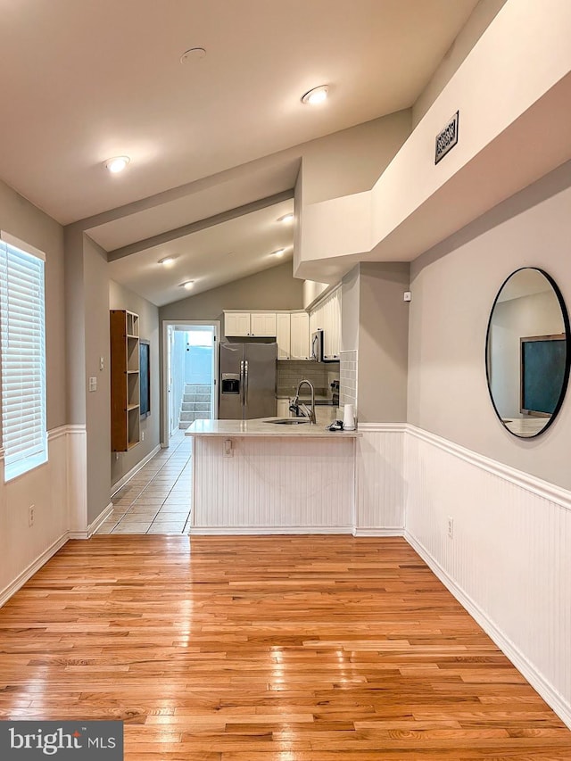 kitchen featuring tasteful backsplash, white cabinetry, kitchen peninsula, light hardwood / wood-style flooring, and stainless steel appliances