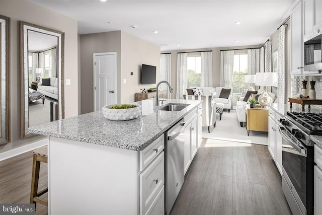 kitchen with a center island with sink, sink, stainless steel appliances, a kitchen bar, and white cabinetry