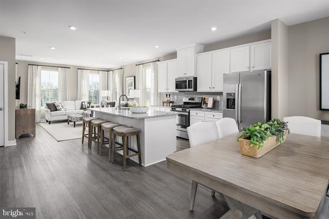 kitchen featuring an island with sink, stainless steel appliances, white cabinets, dark hardwood / wood-style flooring, and a breakfast bar area