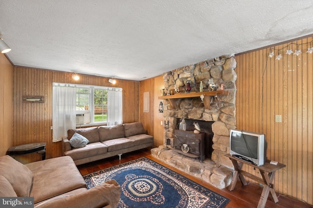 living room featuring wood-type flooring, wooden walls, a stone fireplace, and a textured ceiling