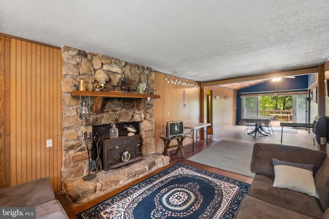 living room with wooden walls, a stone fireplace, a textured ceiling, and vaulted ceiling