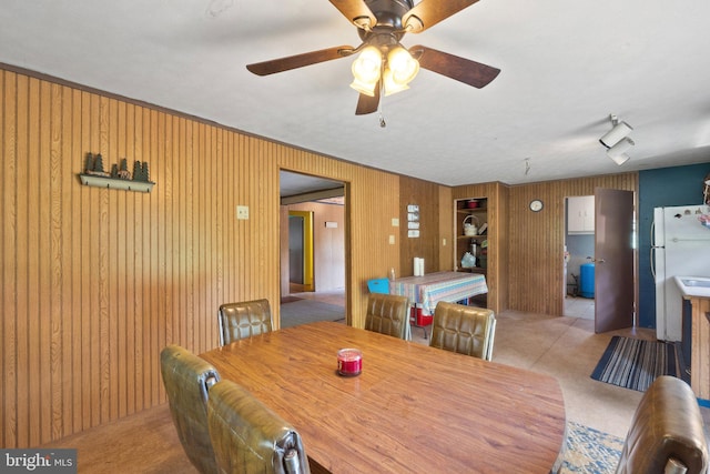 carpeted dining space featuring wooden walls, track lighting, and ceiling fan