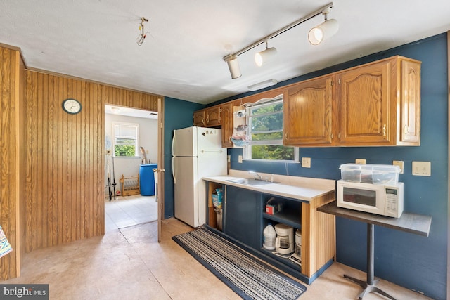 kitchen featuring white appliances, sink, track lighting, and wood walls