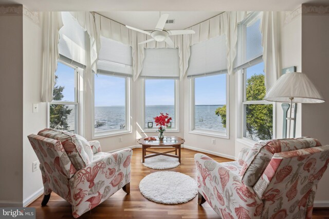 sunroom with ceiling fan and a water view